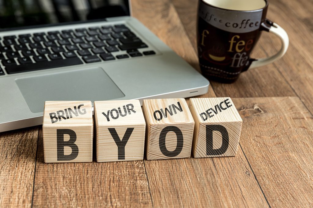 Wooden blocks that spell out BYOD on the front with the words Bring Your Own Device printed on top of them. A laptop is in the background.