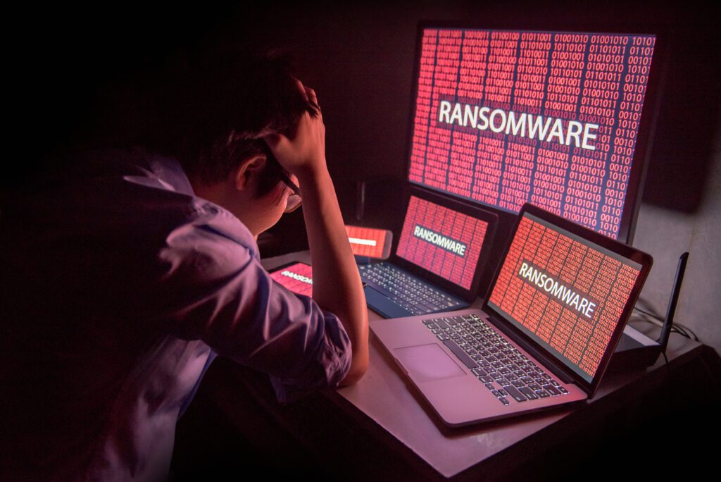 A frustrated and confused person looking at a ransomware attack on their laptop and desktop screens.