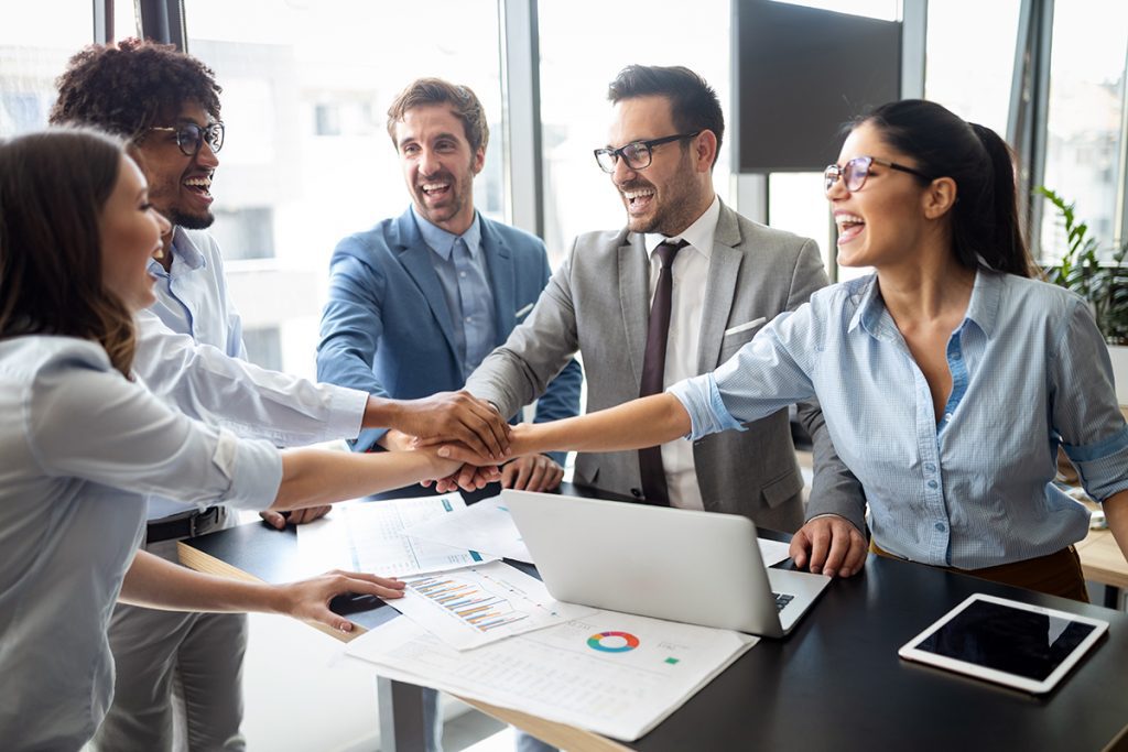A group of coworkers put their hands in the middle of a circle to celebrate success.