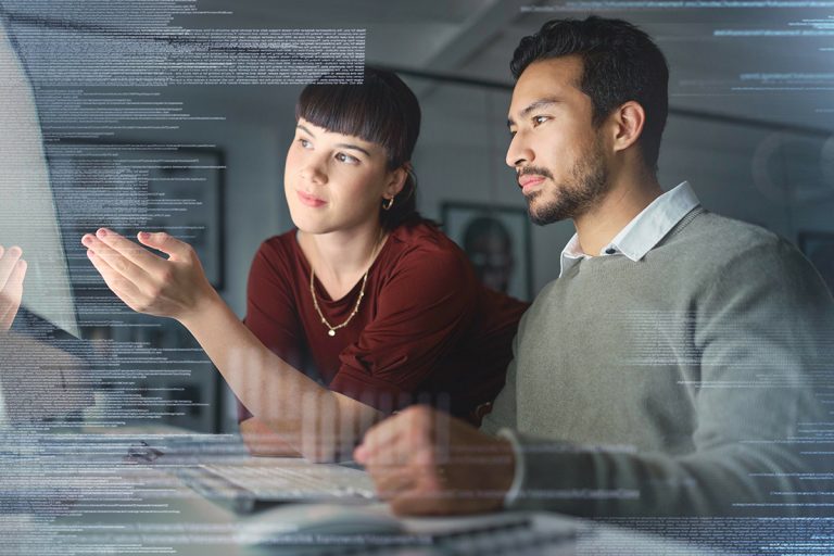 A woman points at a computer screen while a man watches.