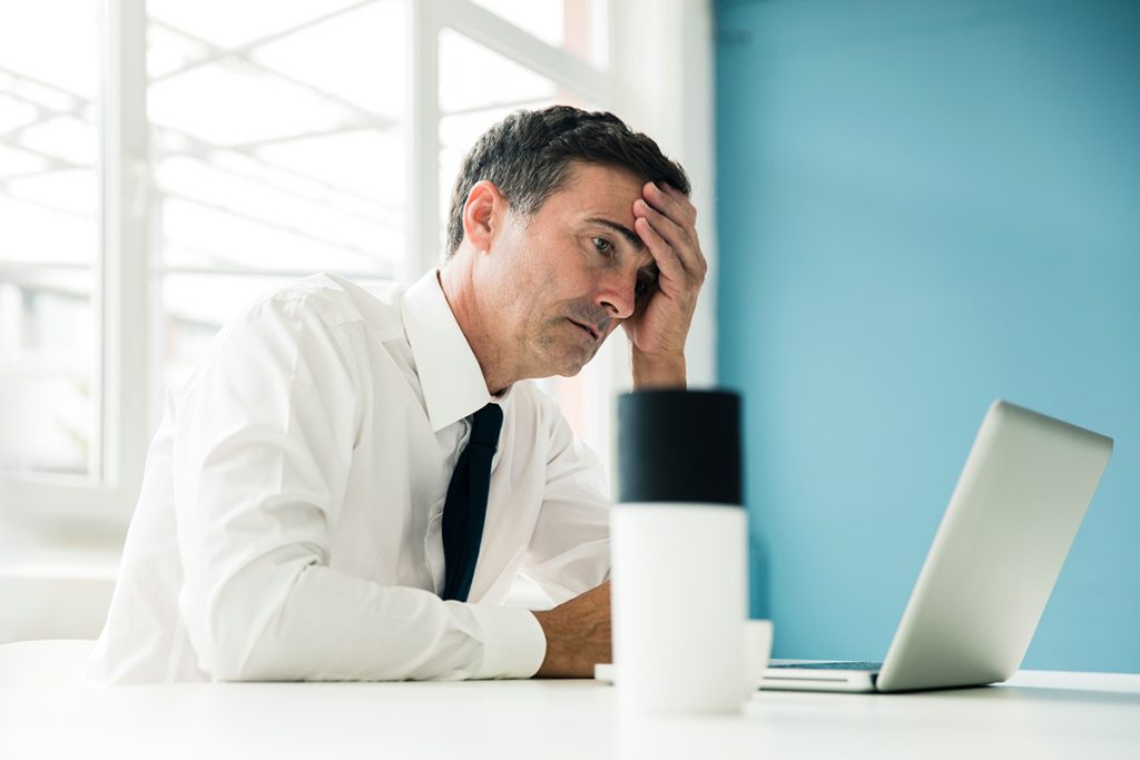 A man in a business suit looks at his laptop with a troubled and puzzled look on his face.