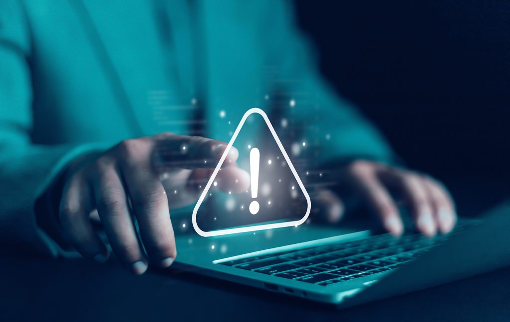 A hand pointing towards a warning symbol superimposed over a laptop.